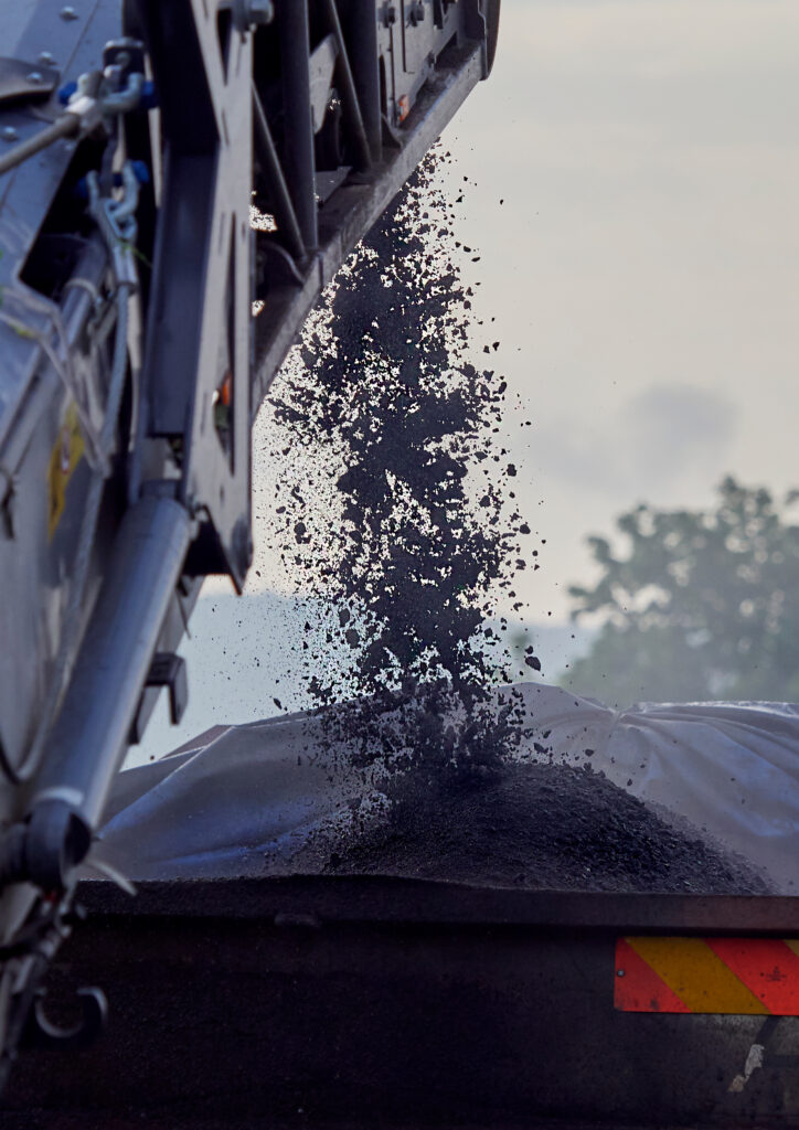 Asphalt millings falling from machinery into a truck bed during roadwork.